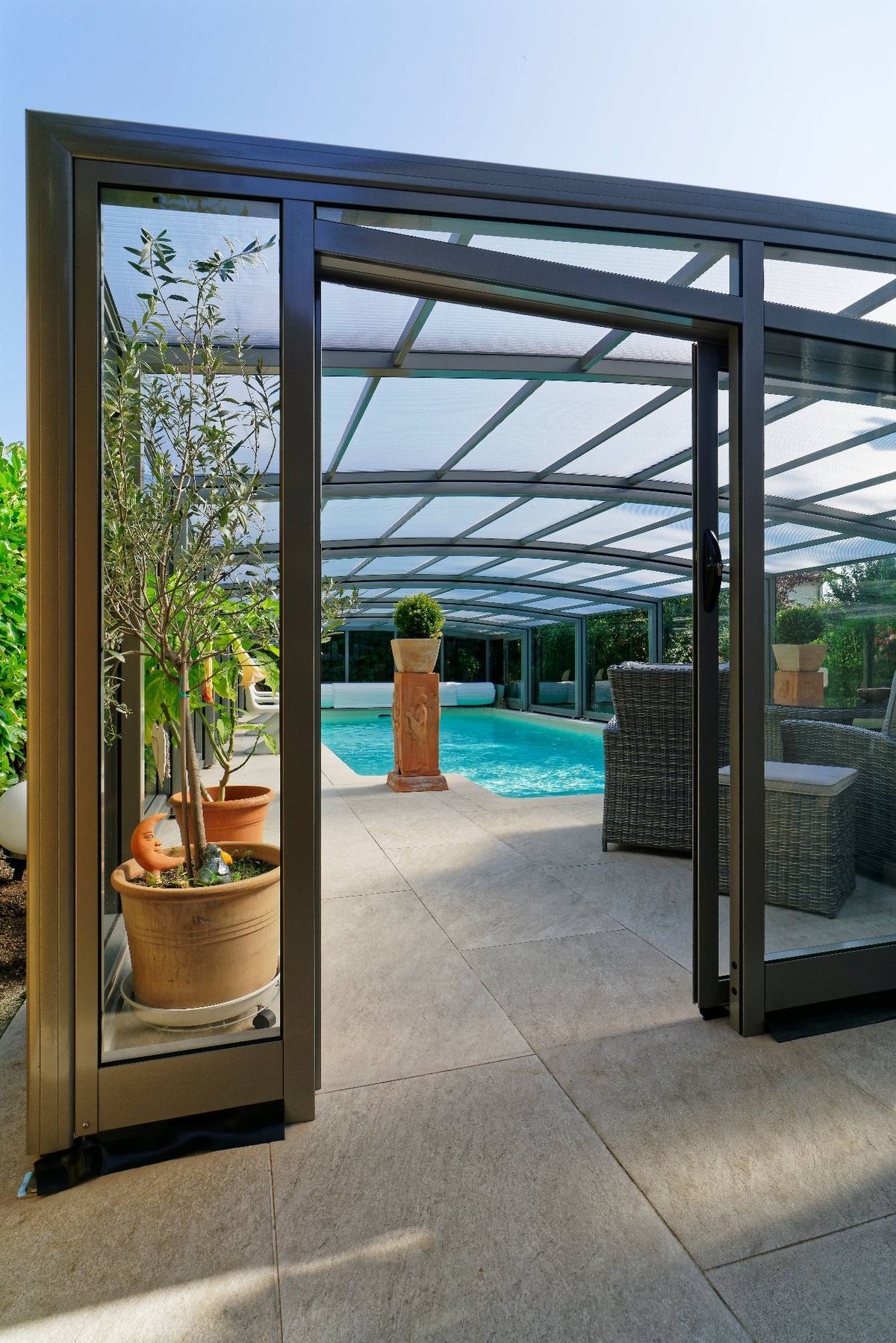 Geöffnete Glastür einer Poolüberdachung mit Blick auf Pool und Sitzbereich mit Pflanzen